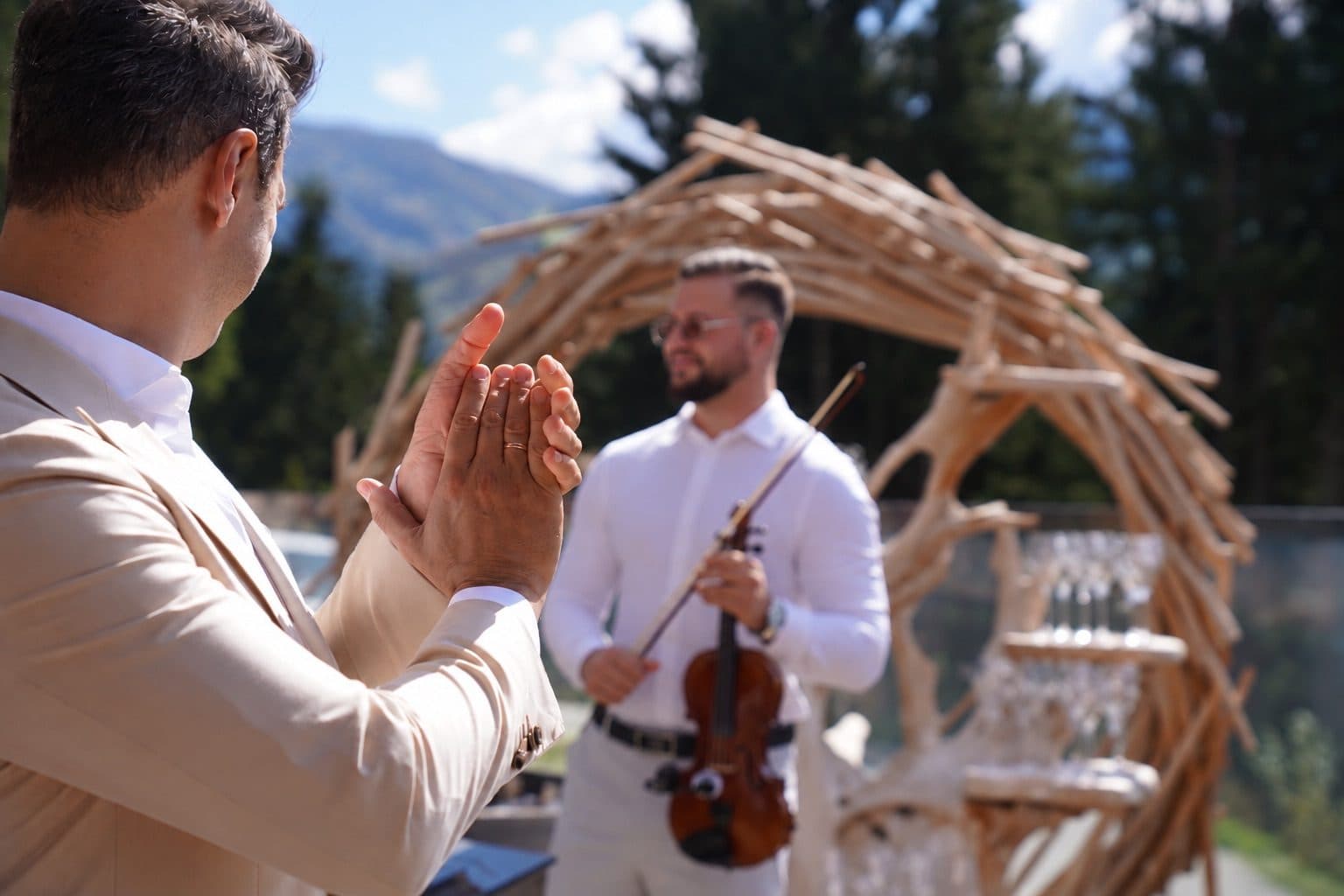 Rauf Schäffer mit Violine unter einem Holzbogen bei einer Hochzeit in den Bergen, ein Gast applaudiert